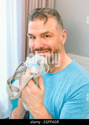 Reifer glücklicher Mann mit chronischen Atemproblemen erwägt die Verwendung CPAP-Maschine auf dem Bett im Schlafzimmer sitzen. Gesundheitswesen, CPAP, Schnarchen Konzept Stockfoto