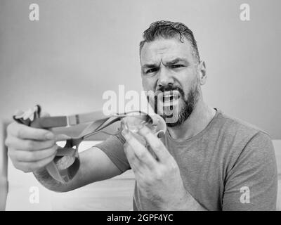 Unglücklich schockiert Mann mit chronischen Atemproblemen überrascht, indem CPAP-Maschine auf dem Bett im Schlafzimmer sitzen. Stockfoto