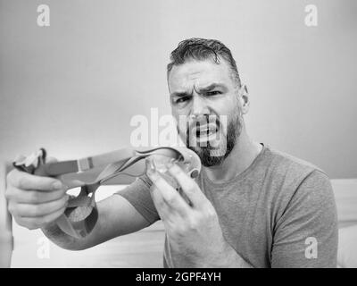 Unglücklich schockiert Mann mit chronischen Atemproblemen überrascht, indem CPAP-Maschine auf dem Bett im Schlafzimmer sitzen. Stockfoto