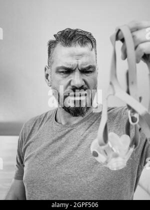 Unglücklich schockiert Mann mit chronischen Atemproblemen überrascht, indem CPAP-Maschine auf dem Bett im Schlafzimmer sitzen. Stockfoto