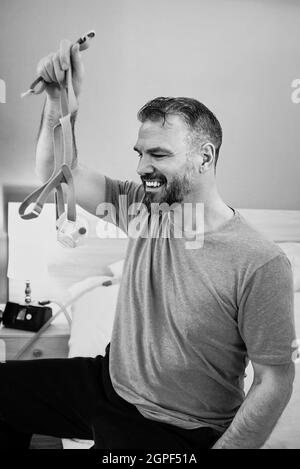 Unglücklich schockiert Mann mit chronischen Atemproblemen überrascht, indem CPAP-Maschine auf dem Bett im Schlafzimmer sitzen. Stockfoto