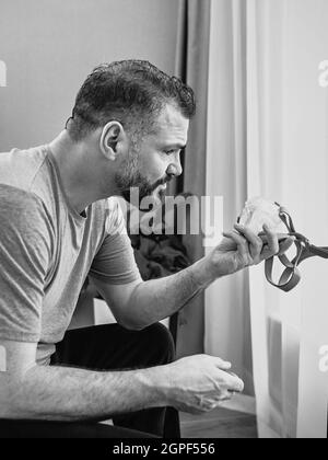 Monochromes Porträt eines glücklichen ausgeruhten Mannes mit chronischen Atemproblemen nach der Verwendung eines CPAP-Geräts, das im Schlafzimmer auf dem Bett sitzt. Gesundheitswesen, CPAP Stockfoto