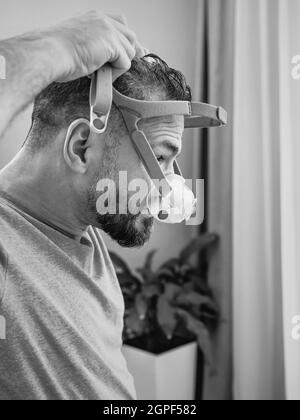 Unglücklich schockiert Mann mit chronischen Atemproblemen überrascht, indem CPAP-Maschine auf dem Bett im Schlafzimmer sitzen. Stockfoto