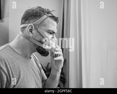 Unglücklich schockiert Mann mit chronischen Atemproblemen überrascht, indem CPAP-Maschine auf dem Bett im Schlafzimmer sitzen. Stockfoto