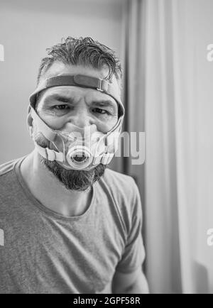 Unglücklich schockiert Mann mit chronischen Atemproblemen überrascht, indem CPAP-Maschine auf dem Bett im Schlafzimmer sitzen. Stockfoto