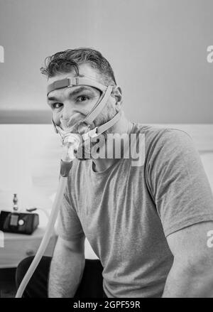 Unglücklich schockiert Mann mit chronischen Atemproblemen überrascht, indem CPAP-Maschine auf dem Bett im Schlafzimmer sitzen. Stockfoto