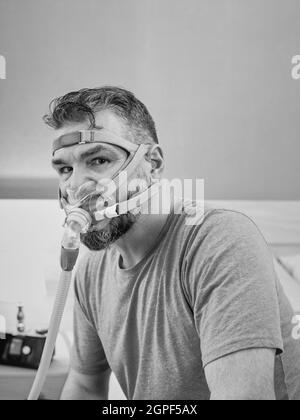 Unglücklich schockiert Mann mit chronischen Atemproblemen überrascht, indem CPAP-Maschine auf dem Bett im Schlafzimmer sitzen. Stockfoto