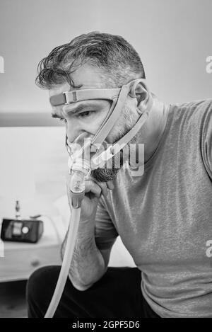 Unglücklich schockiert Mann mit chronischen Atemproblemen überrascht, indem CPAP-Maschine auf dem Bett im Schlafzimmer sitzen. Stockfoto