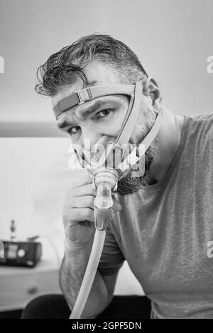 Unglücklich schockiert Mann mit chronischen Atemproblemen überrascht, indem CPAP-Maschine auf dem Bett im Schlafzimmer sitzen. Stockfoto