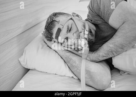 Monochromes Porträt eines schlafenden Mannes mit chronischen Atemproblemen erwägt die Verwendung des CPAP-Geräts im Bett. Gesundheitswesen, obstruktive Schlafapnoe-Therapie Stockfoto
