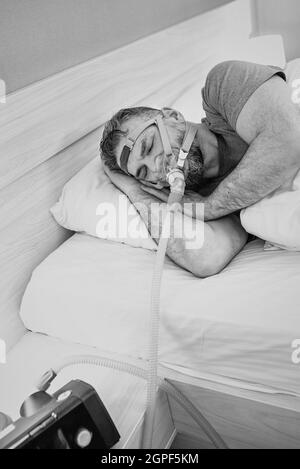 Monochromes Porträt eines schlafenden Mannes mit chronischen Atemproblemen erwägt die Verwendung des CPAP-Geräts im Bett. Gesundheitswesen, obstruktive Schlafapnoe-Therapie Stockfoto
