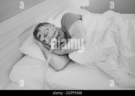 Monochromes Porträt eines schlafenden Mannes mit chronischen Atemproblemen erwägt die Verwendung des CPAP-Geräts im Bett. Gesundheitswesen, obstruktive Schlafapnoe-Therapie Stockfoto