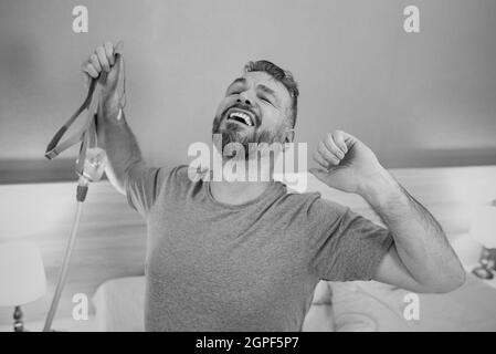 Monochromes Porträt eines glücklichen ausgeruhten Mannes mit chronischen Atemproblemen nach der Verwendung eines CPAP-Geräts, das im Schlafzimmer auf dem Bett sitzt. Gesundheitswesen, CPAP Stockfoto