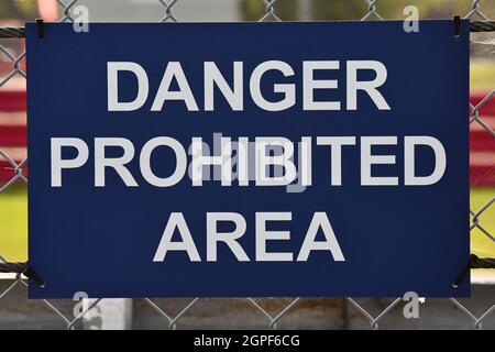 Ein blaues Schild mit weißer Schrift, das an einen Sicherheitszaun geschnallt ist und einen Gefahrenbereich angibt Stockfoto