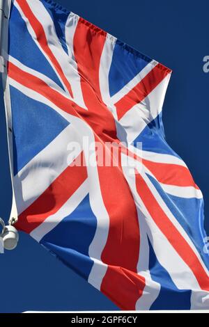 Eine vertikale Union Jack-Flagge auf einem Fahnenmast, der im Wind weht, mit dem Hintergrund eines klaren blauen Himmels, der die britische Flagge gegen den blauen Himmel schwenkt Stockfoto