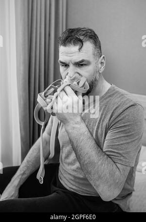 Unglücklich schockiert Mann mit chronischen Atemproblemen überrascht, indem CPAP-Maschine auf dem Bett im Schlafzimmer sitzen. Stockfoto