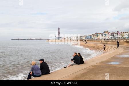 Touristen sitzen an der Strandverteidigung von Blackpool und beobachten, wie die Flut im September 2021 ausgeht. Stockfoto