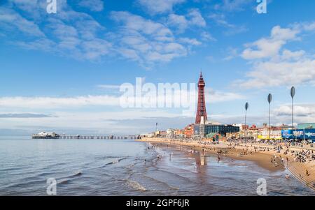 Touristen kommen ins Wasser, wenn die Flut im September 2021 am Strand von Blackpool ausbricht. Der North Pier und der Blackpool Tower nehmen den Hintergrund ein Stockfoto