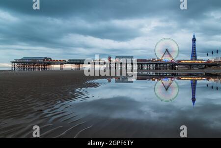 Eine lange Exposition des Riesenrads, das sich am Central Pier am Blackpool Beach dreht, gesehen in der Dämmerung im September 2021, als der Blackpool Tower beleuchtet wird Stockfoto