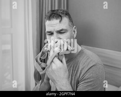 Unglücklich schockiert Mann mit chronischen Atemproblemen überrascht, indem CPAP-Maschine auf dem Bett im Schlafzimmer sitzen. Stockfoto