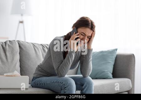 Verzweiflung verärgerte kaukasische tausendjährige Frau, die an Depressionen leidet, zu Hause weint und telefoniert Stockfoto