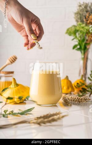 Ein natürlicher Smoothie aus gelbem Kürbis. Herbstgetränk mit Honig und Milch. Auf hellem Hintergrund, senkrechte Position Stockfoto