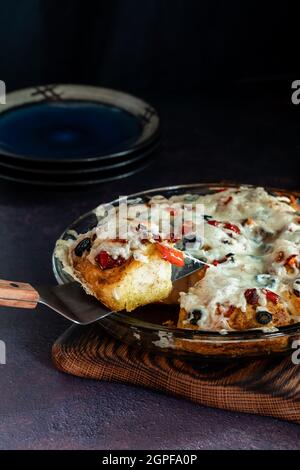 Hausgemachte Pizza Ziehen Sie Brot mit einem Stück auf einem Spatel, vor einem dunklen Hintergrund. Stockfoto