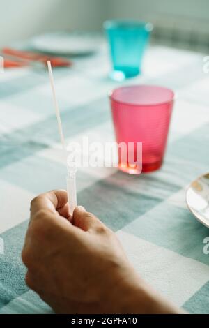 Ein junger Kaukasusmann hält eine Pipette in der Hand mit einem Nasopharyngealabstrich und einer eigenen Probe hinein, während er eine Covid-19-Antigendiagnose nimmt Stockfoto