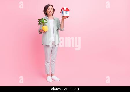 Ganzkörper-Porträt der fröhlichen froh Person halten Pflanze Mini-Haus haben gute Laune auf rosa Hintergrund isoliert Stockfoto