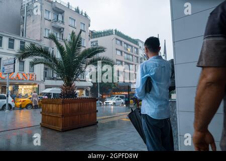 Beyoglu, Istanbul, Türkei - 06.18.2021: Ein Mann, der vor einer Gebäudesäule steht, während es draußen in Taksim mit starken Regenfällen regnet Stockfoto