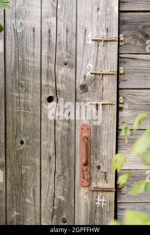 Tür einer alten hölzernen Toilette oder Scheune mit einem rostigen Türknauf und drei Verriegelungen, in einer Landschaft. Stockfoto