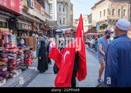 Eminonu, Istanbul, Türkei - 07.05.2021: Ein bärtiger alter Mann mit grauem Haar, der türkische Flaggen verkauft und die Kamera auf dem Mahmutpasa Basar Open Market anschaut Stockfoto