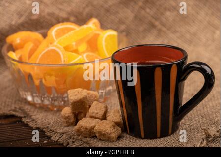 Bunte, geformte Marmeladenscheiben in einer Glasvase, Stücke braunen Rohrzuckers und eine Tasse Kaffee, Nahaufnahme, selektiver Fokus Stockfoto