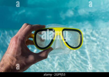 Gelbe Schwimmbrille neben einem klaren, blau gewellten Swimmingpool Stockfoto