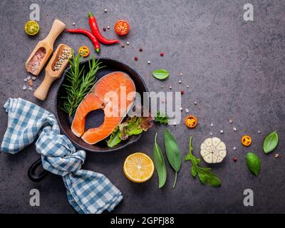 Lachsfilet in alten Gusseisen skille auf dunklem Stein Hintergrund. Zutaten für die Herstellung von steak Konzept mit kopieren. Verschiedene Kräuter und Gewürze rose Stockfoto