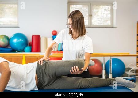 Weibliche Physiotherapeutin, die bei einem männlichen Patienten eine Bein- und Hüftstreckungs-Behandlung macht. Stockfoto