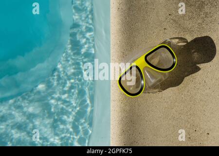 Gelbe Schwimmbrille neben einem klaren, blau gewellten Swimmingpool Stockfoto