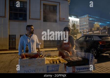 Beyoglu, Istanbul, Türkei - 07.07.2021: Zwei Händler frittieren an einem Sommertag nachts auf einem tragbaren mangal-Grill in der Karakoy-Straße Fisch zur Zubereitung Stockfoto