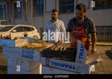 Beyoglu, Istanbul, Türkei - 07.07.2021: Zwei männliche Händler braten an einem tragbaren mangal-Grill in der Karakoy-Straße nachts an einem Sommertag Fisch Stockfoto