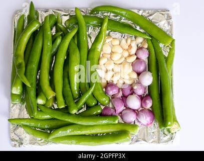 Draufsicht auf rohes grünes Chili, Knoblauch und Zwiebel auf Aluminiumfolie, bevor es zum Backen in den Ofen gegeben wird. Vollformat-Foto auf weißem Hintergrund mit Kopie sp Stockfoto