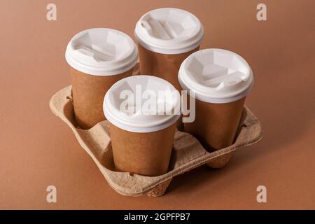 Pappbecher in einem Tassenhalter für Kaffee zum Mitnehmen. Pappbecher mit einem Getränk. Einweggeschirr. Recycelbarer Öko-Karton. Brauner Hintergrund. Speicherplatz kopieren. Frühstück wird ins Büro gebracht. Stockfoto