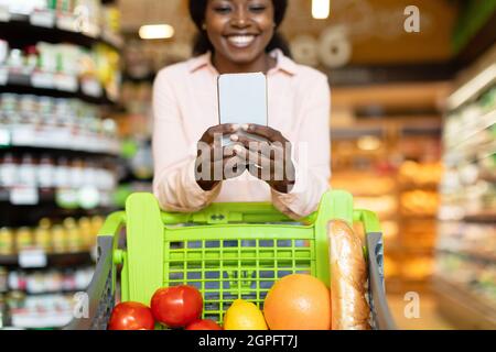 Happy Black Woman Einkaufen Lebensmittel Auf Smartphone In Supermarkt Stockfoto