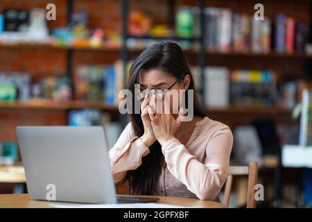 Erschöpfte Freiberuflerin mit Sehproblemen während der Arbeit an einem Laptop im Café, leiden unter Schmerzen und Müdigkeit Stockfoto