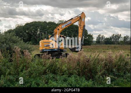 Ein Bagger, der Abflussgräben auf niedrig gelegenen grasenden Sumpfschümpfen auf den Norfolk Broads bei Buckenham Marshes beibehält Stockfoto