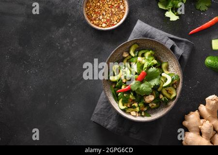 Asiatischer würziger, gebrochener Gurkensalat mit Koriander, Ingwer, Pfeffer-Chili, schwarzem Essig auf schwarzem Hintergrund. Speicherplatz kopieren. Würzige Gurken. Stockfoto