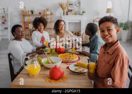 Lächelnder afroamerikanischer Junge mit Orangensaft in der Nähe der Familie beim Danksageessen Stockfoto