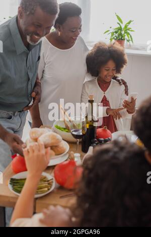 afroamerikanisches Kind mit Smartphone in der Nähe von Großeltern und Danksagungs-Dinner Stockfoto