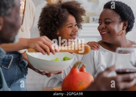 Lächelndes afroamerikanisches Mädchen umarmte Großmutter während des Danksagender-Abendessens Stockfoto