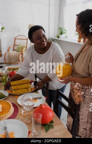 afroamerikanische Frau, die Mais mit Orangensaft auf den Esstisch neben der Tochter legte Stockfoto