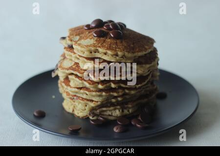 Stapel von Hafer Choco Chips Pfannkuchen zusammen mit Kaffee zum Frühstück. Gesunde Pfannkuchen aus Hafermehl mit Schokoladensplittern. Auf weißem Bac geschossen Stockfoto